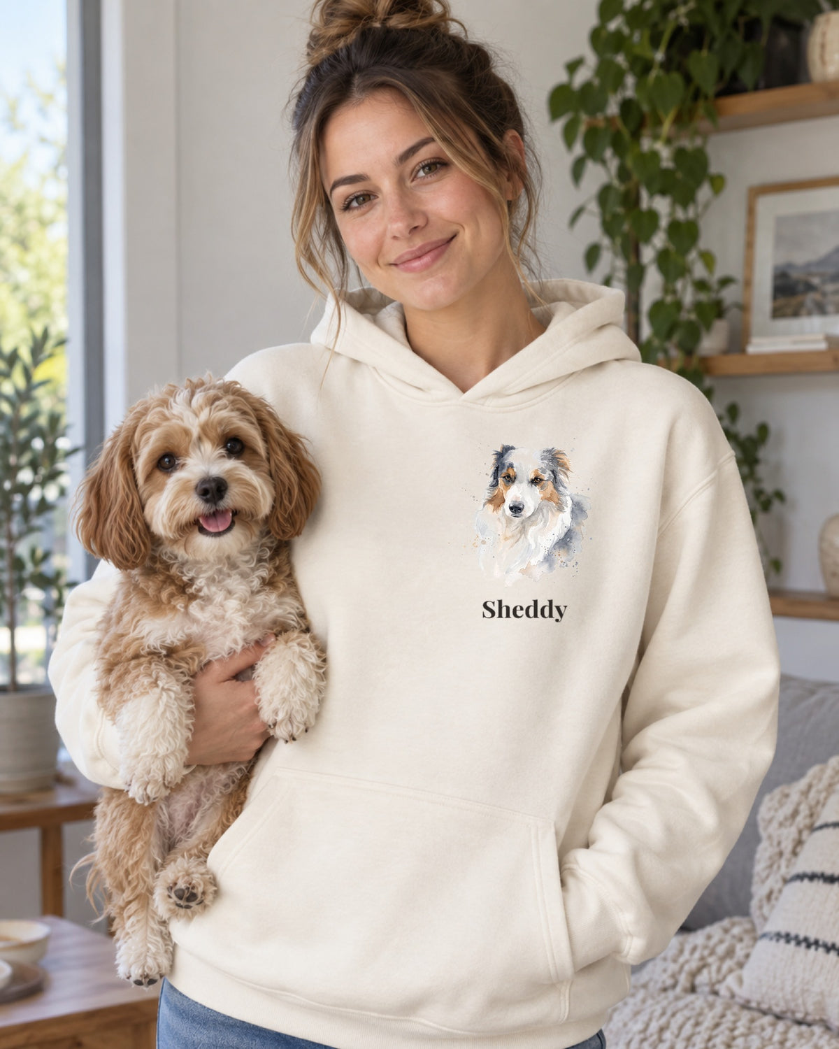 Hoodie in Creme mit Hundeportrait im Stil Aquarell und dem Namen Sheddy, getragen von einer Frau mit ihrem Hund auf dem Arm