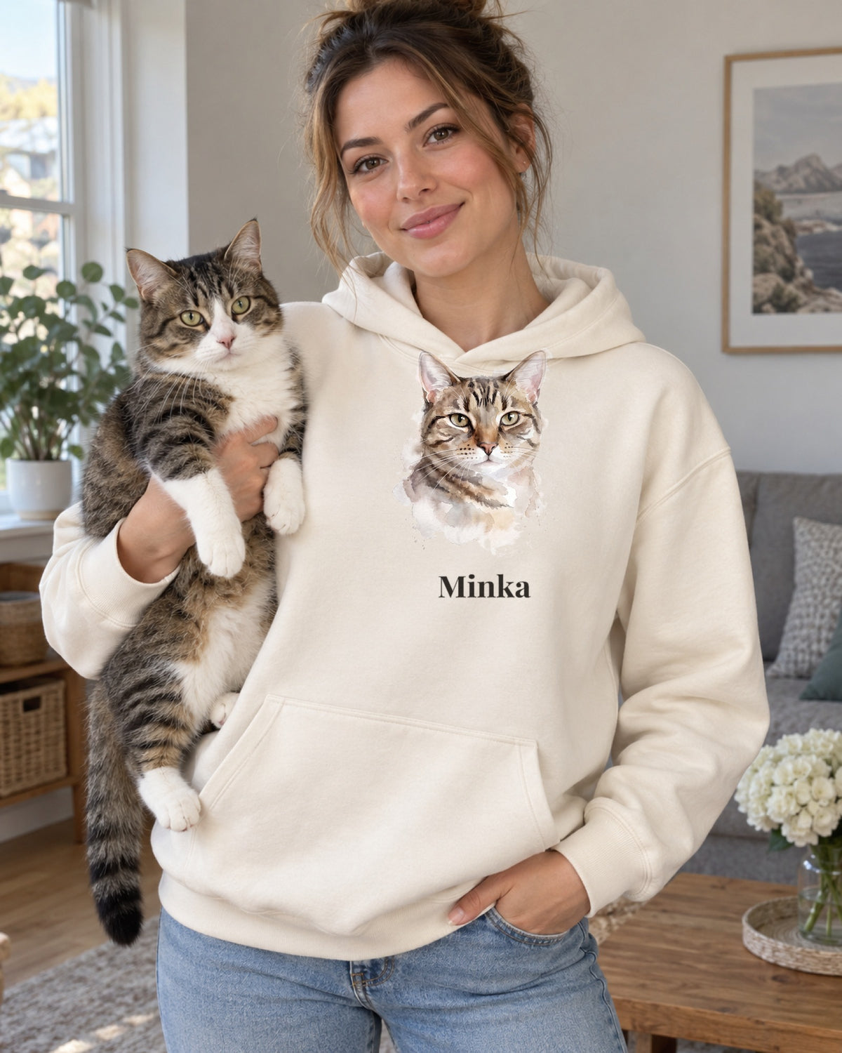 Hoodie in Creme mit Katzenportrait im Stil Aquarell und dem Namen Minka, getragen von einer Frau mit ihrer Katze auf dem Arm