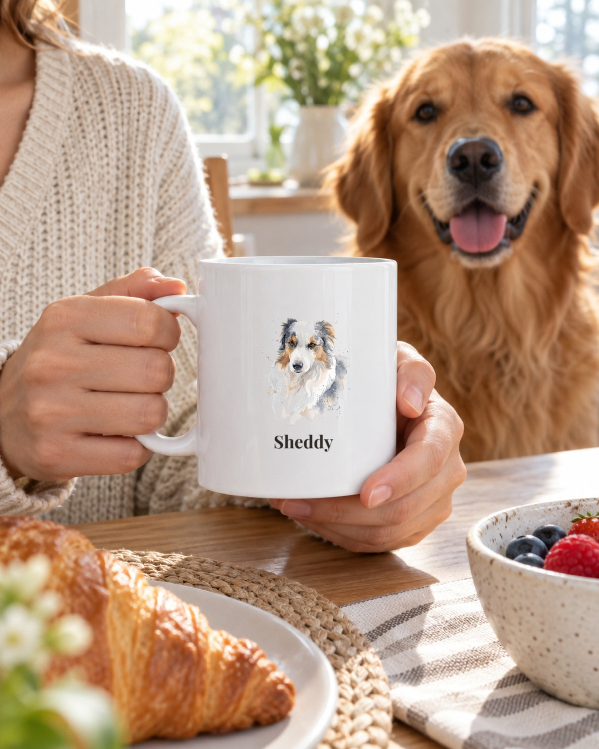 Weiße Tasse mit Hundeportrait im Stil Aquarell und dem Namen Sheddy, von einer Frau gehalten, ein Golden Retriever sitzt dahinter