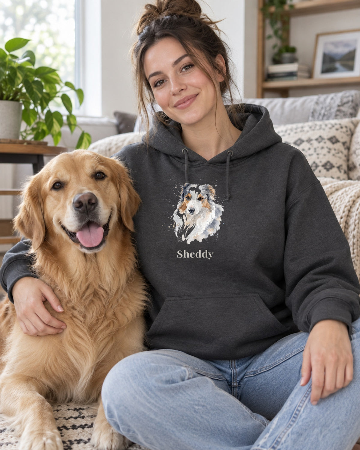 Hoodie in Dunkelgrau mit Hundeportrait im Stil Aquarell und dem Namen Sheddy, getragen von einer Frau mit ihrem Hund auf dem Sofa