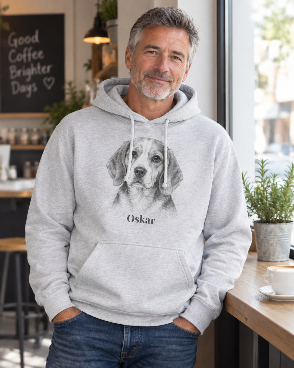 Mann im hellgrau melierten Hoodie mit Beagle im Sketch Stil und dem Namen Oskar an einem Fenster im Café