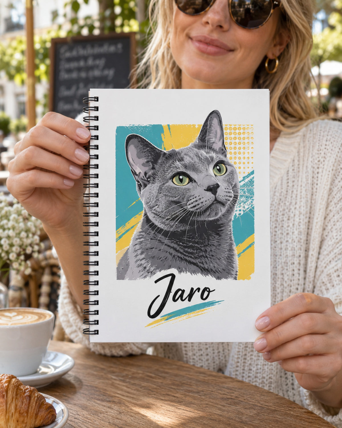 Frau hält Notizbuch mit Kartäuserkatze im Pop-Art-Stil und Namen Jaro