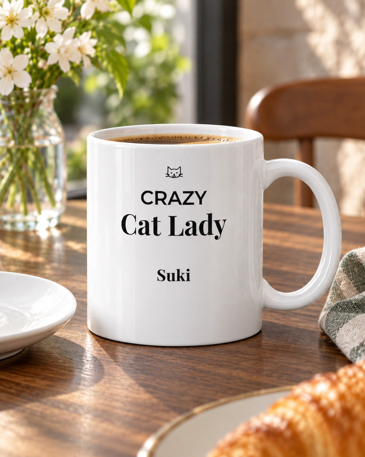 Weiße Keramiktasse Crazy Cat Lady Tasse mit Namen deiner Katze auf einem Cafétisch im Frühling mit Beispielname Suki