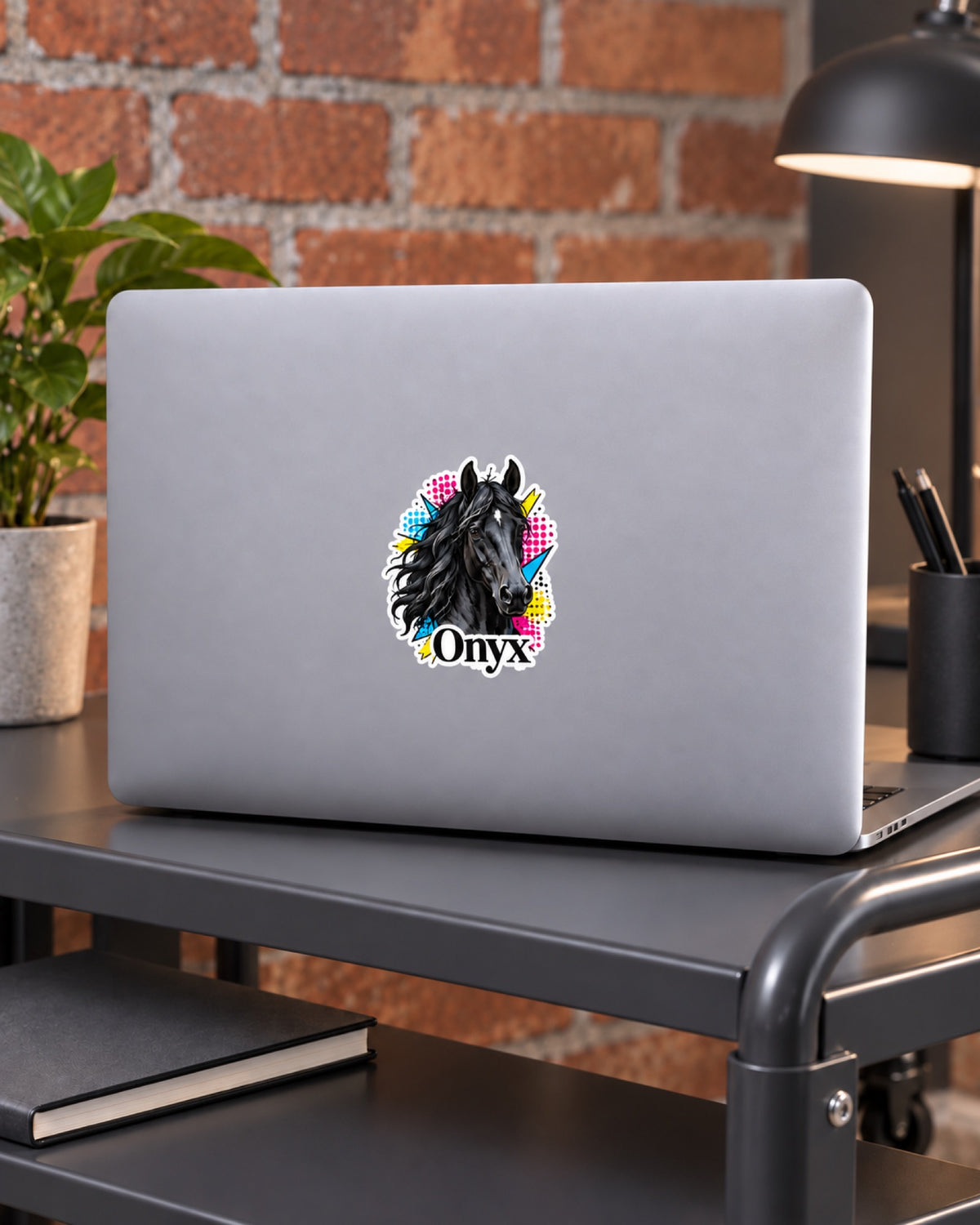Vinylsticker 7,6 cm mit Rappe im Pop Art Stil und Namen Onyx auf einem grauen Laptop auf einem dunkelgrauen Rollschreibtisch vor Ziegelwand