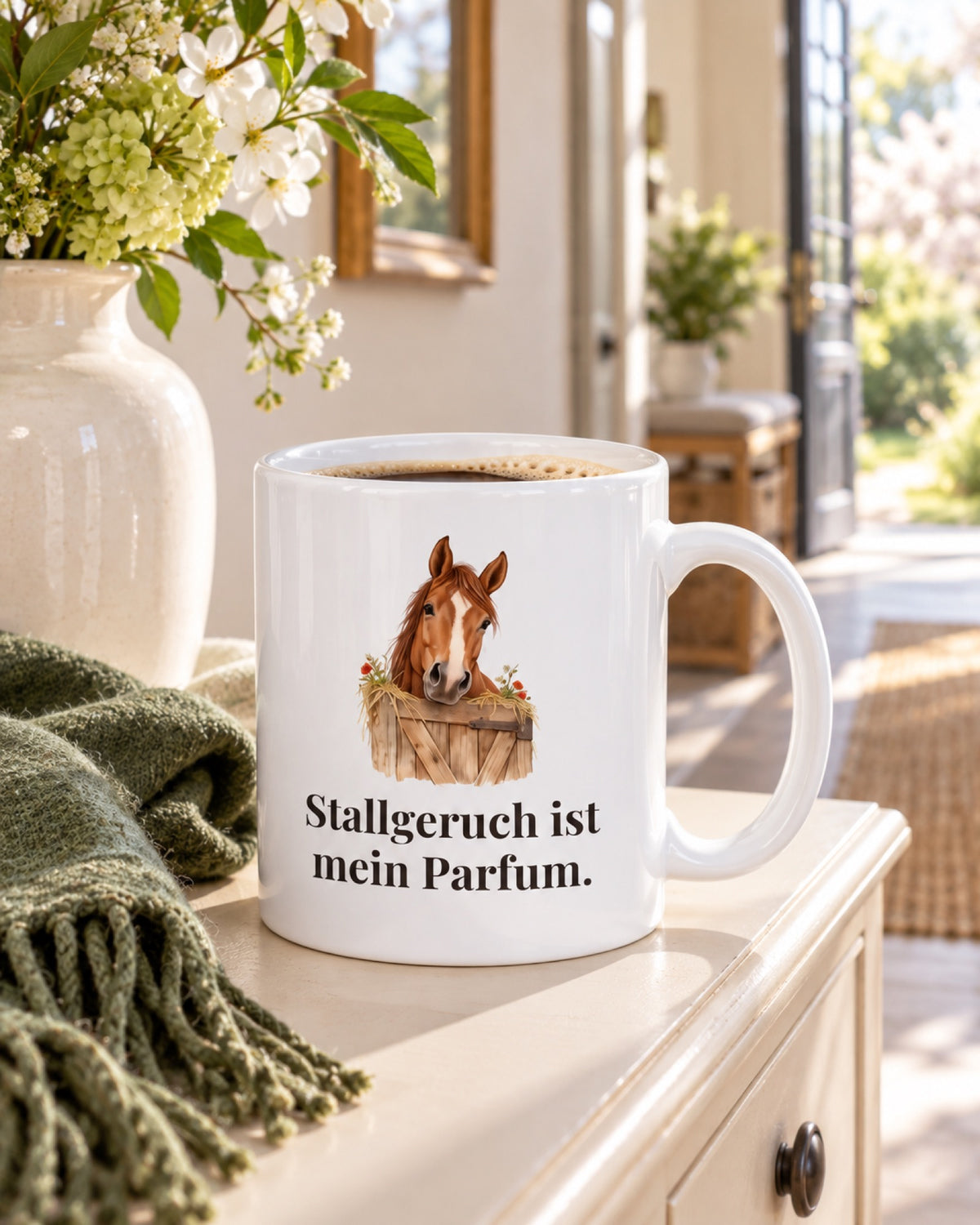 Weiße Keramiktasse Pferdetasse mit Spruch: Stallgeruch ist mein Parfum. auf einer cremefarbenen Konsolenablage