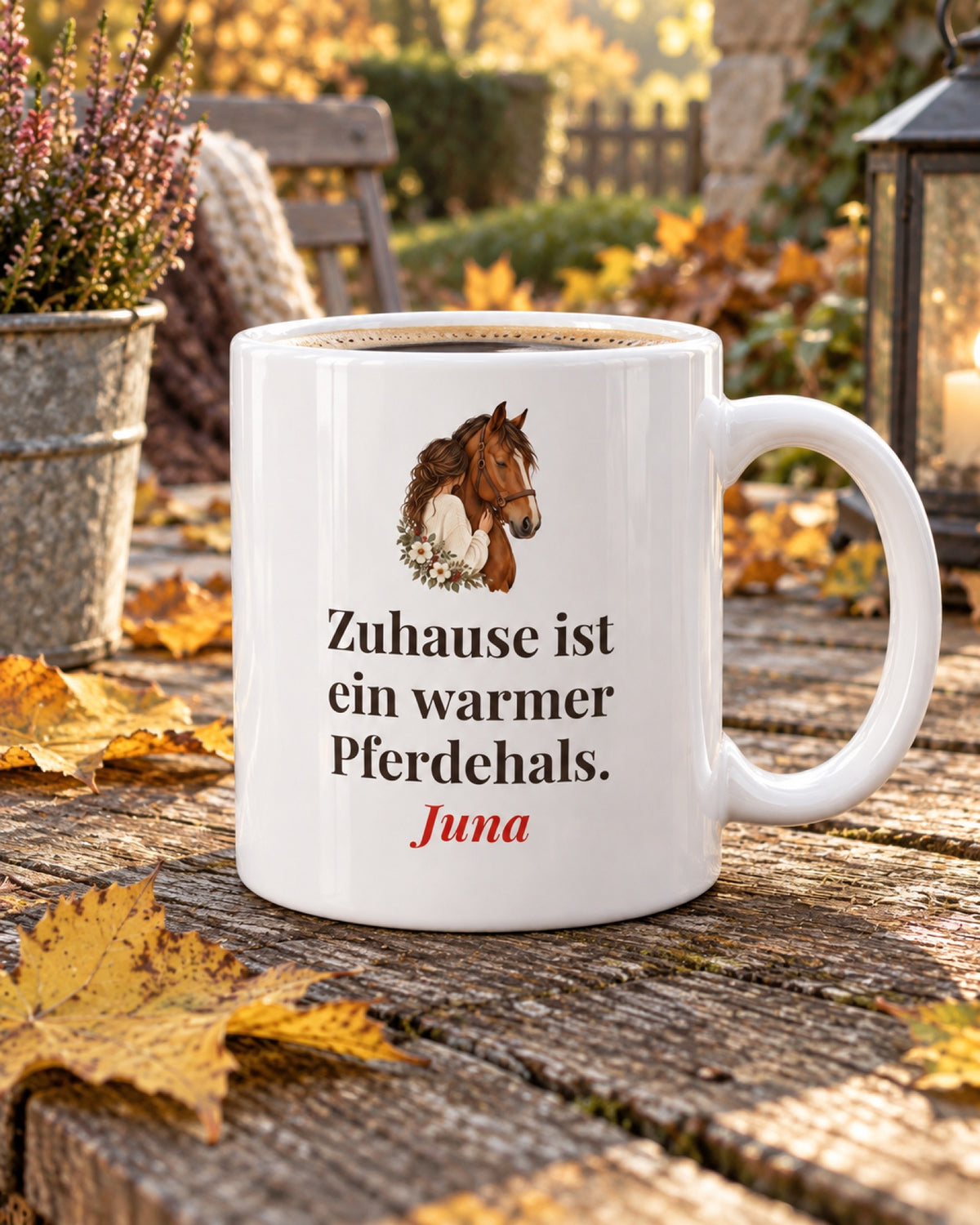 Weiße Keramiktasse Pferdetasse mit Spruch: Zuhause ist ein warmer Pferdehals. auf einem Gartentisch im Herbst mit Beispielname Juna
