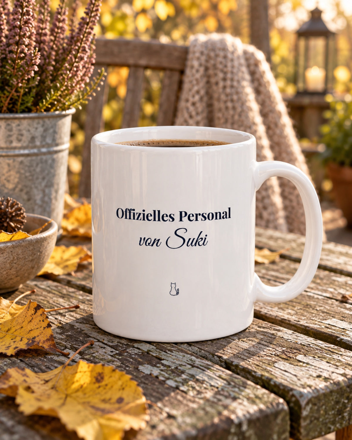 Weiße Keramiktasse Spruchtasse für Katzenmenschen auf einem Gartentisch im Herbst mit Beispielname Suki