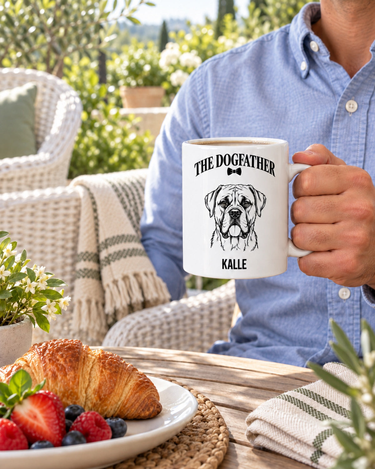Tasse The Dogfather mit Boxer Kalle in der Hand auf einer sommerlichen Gartenterrasse