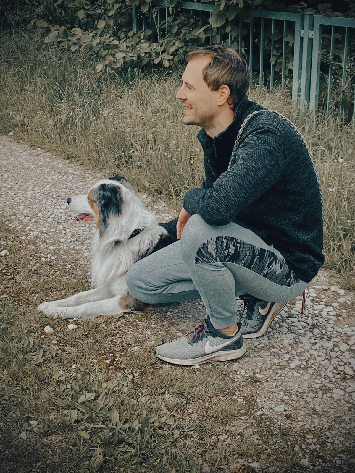 Tobi von PrintMyPet hockt auf einem Feldweg neben seinem Hund Sheddy, einem Mix aus Australian Shepherd und Border Collie